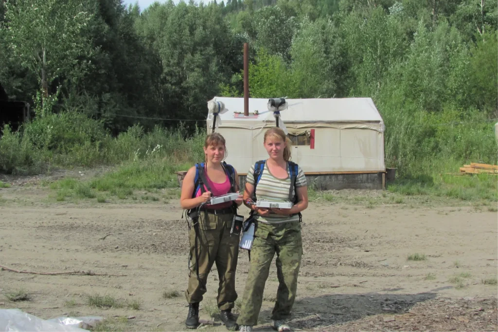 Две участницы геофизической экспедиции перед выходом на маршрут. Слева – главный редактор Мария Костина, обе держат управляющие блоки, за спиной – датчики магнитометра. На фоне – палатка полевого лагеря.