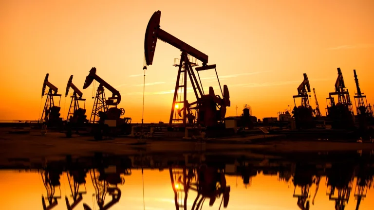 Силуэты нефтяных вышек на фоне закатного неба, отражающиеся в воде