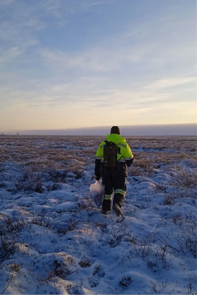 Специалист в защитной одежде идёт по зимнему тундровому ландшафту во время полевых геофизических работ