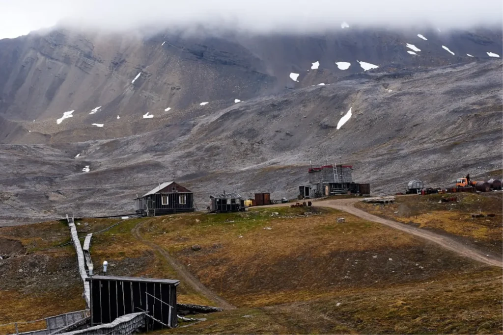 Арктическая научная станция среди гор, с деревянными постройками и техникой на фоне туманных склонов