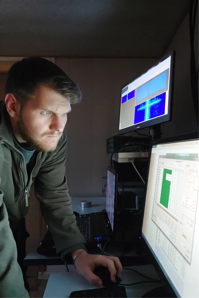 Инженер-геофизик анализирует данные на нескольких мониторах в полевой лаборатории