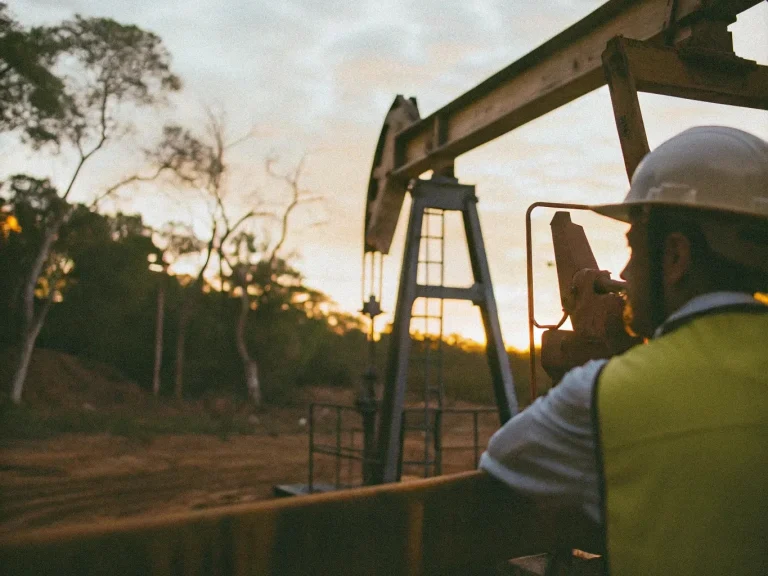 Инженер по нефтяному месторождению наблюдает за работой штангового насоса на фоне заката, иллюстрируя внедрение умных систем управления для снижения износа оборудования