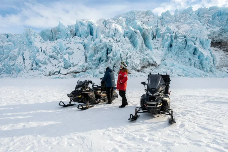 Люди на снегоходах у подножия ледника в Арктике
