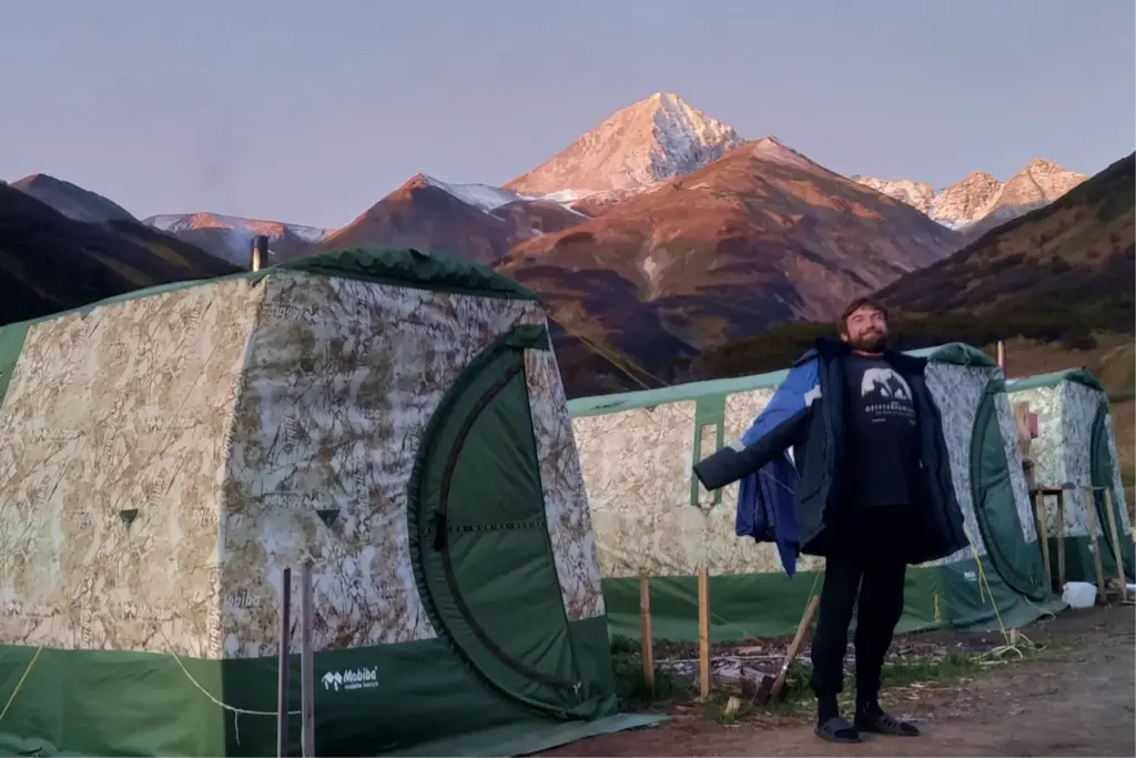 Мужчина в полевом лагере на фоне палаток и гор на Камчатке, утро