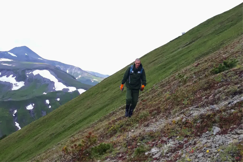 Геолог поднимается по крутому склону в горах Камчатки, чтобы отобрать пробы на одном уровне без перепадов высот