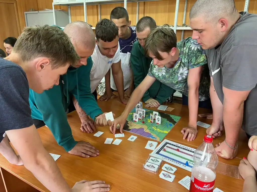 Группа студентов играет в настольную игру с картой и фишками на геологической практике, имитируя рабочие процессы в полевых условиях.