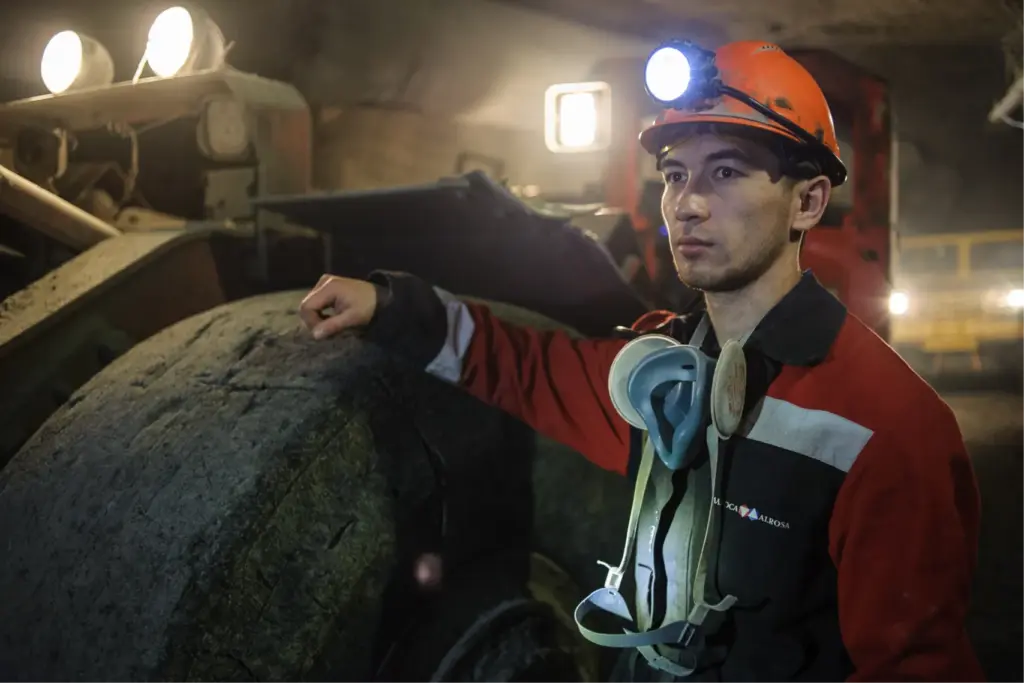 Молодой горняк в каске и с налобным фонарём возле подземной машины в алмазной шахте