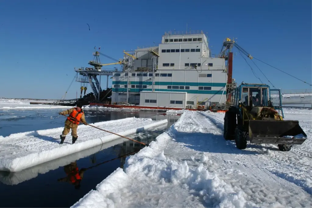 Работник на льду управляет понтоном у драги, ведущей добычу россыпных алмазов в арктических условиях