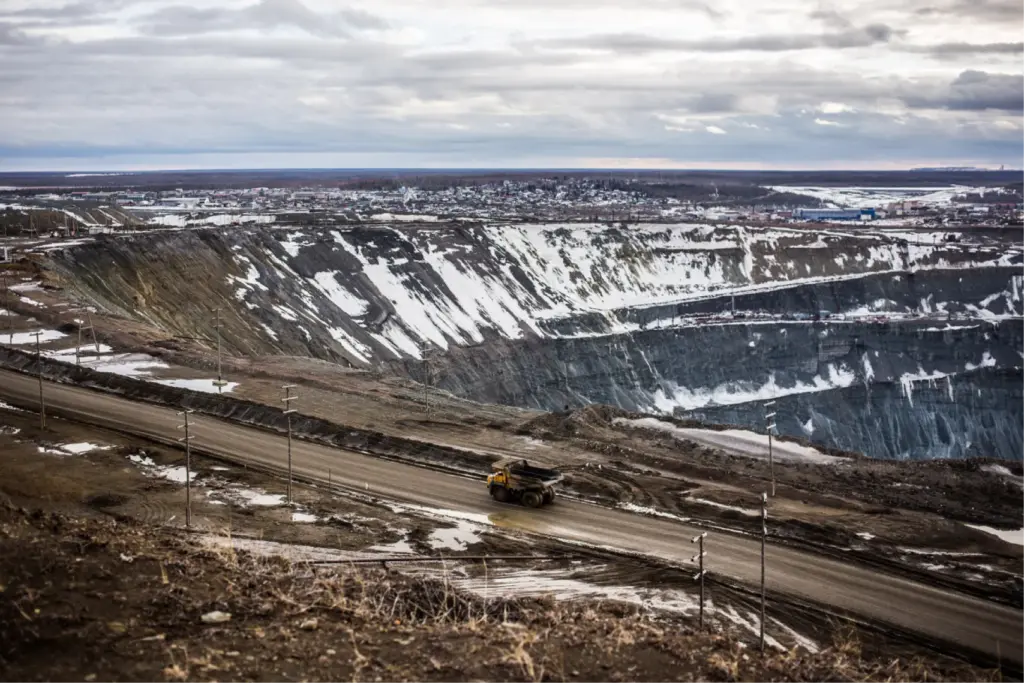 Фотография гигантского алмазного карьера трубки Мир в Мирном (Якутия), глубиной 525 метров и шириной более километра, с техникой на фоне и городом на горизонте