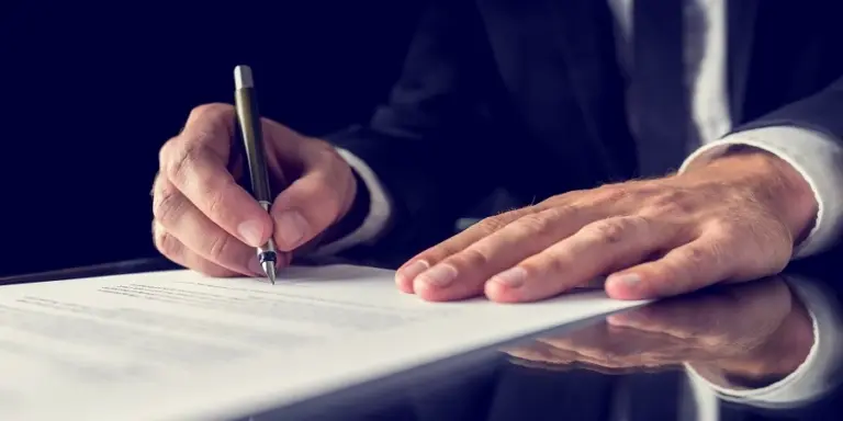 Рука бизнесмена подписывает соглашение о сотрудничестве между БелАЗ и Норникелем по выпуску водородных и аккумуляторных карьерных самосвалов.