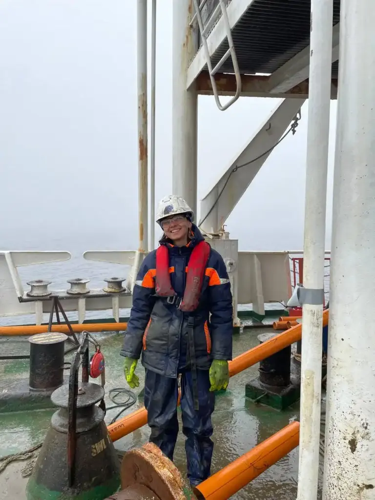 Виктория Меркурьева, геофизик.
Женщина в спасательном жилете и каске стоит на палубе исследовательского судна во время морской геофизической экспедиции. Мокрое оборудование на фоне
