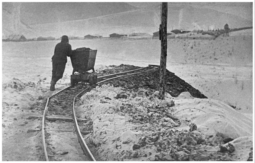 Заключённый ГУЛАГа вручную толкает вагонетку с грунтом по узкоколейной дороге на колымском прииске в 1930–1940-х годах — типичная тяжёлая работа при добыче золота в условиях вечной мерзлоты